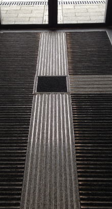 Reinstreifermatte mit optischen und taktilen Kontrasten im Eingangsbereich eines Gebäudes, eingegliedert in ein Blindenleitsystem